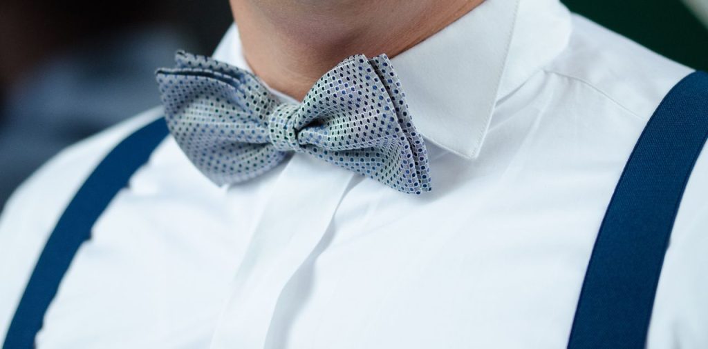 Close-up image of a fashionable bow tie and suspenders on a man wearing a white shirt.